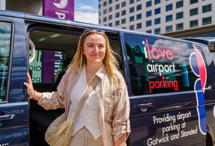 Smiling woman being dropped off at Gatwick Airport by an I Love Park & Deliver transfer bus