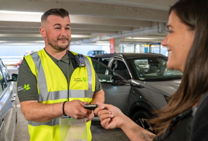 Female passenger handing her car keys to a Maple Parking Meet & Greet South staff member wearing a high-vis jacket with the company logo at Gatwick Airport