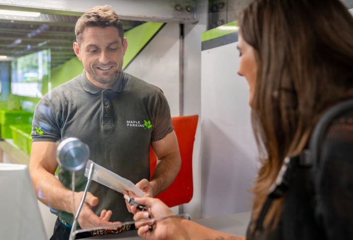 Smiling female passenger handing over her car keys to a male Maple Parking Meet & Greet North staff member wearing a green company logo t-shirt at Gatwick Airport