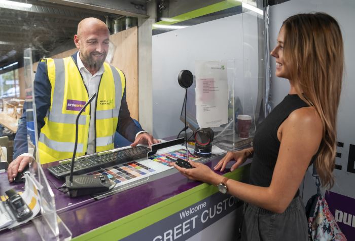 Friendly exchange as a female passenger hands over her keys to a male Purple Parking staff member wearing a high-vis jacket with the company logo at Gatwick South Terminal