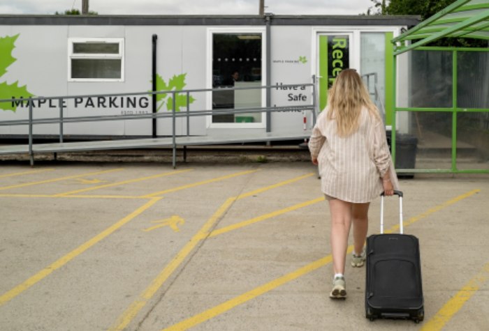 Female customer walking with suitcase through Heathrow Maple Parking Express Park and Ride car park to reception, after dropping off her car