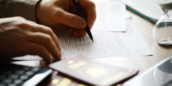 A person’s hands completing a consent form beside two passports and an hourglass, illustrating under 18’s consent form.