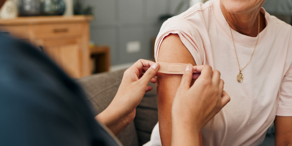 A healthcare professional applying a plaster to a person’s upper arm after vaccination, illustrating vaccines for travel.