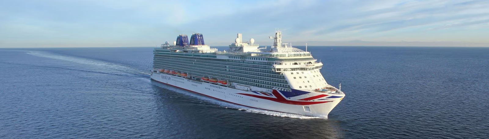 An aerial view of a cruise ship with a large pool deck visible at the rear, and a spacious area with lounge chairs and sunbeds.