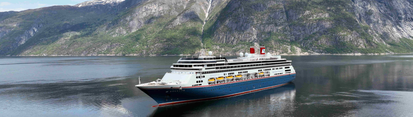 An aerial view of a cruise ship with a large pool deck visible at the rear, and a spacious area with lounge chairs and sunbeds.
