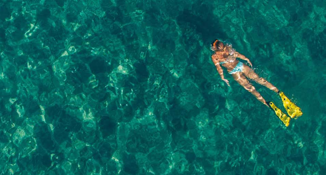 Woman snorkelling in emerald green waters wearing yellow flippers
