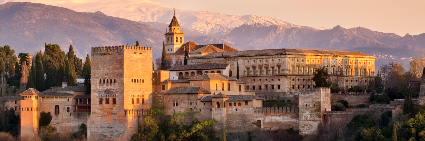 Travel Insurance for Spain – scenic view of the Alhambra in Granada with the Sierra Nevada mountains in the background at sunset.