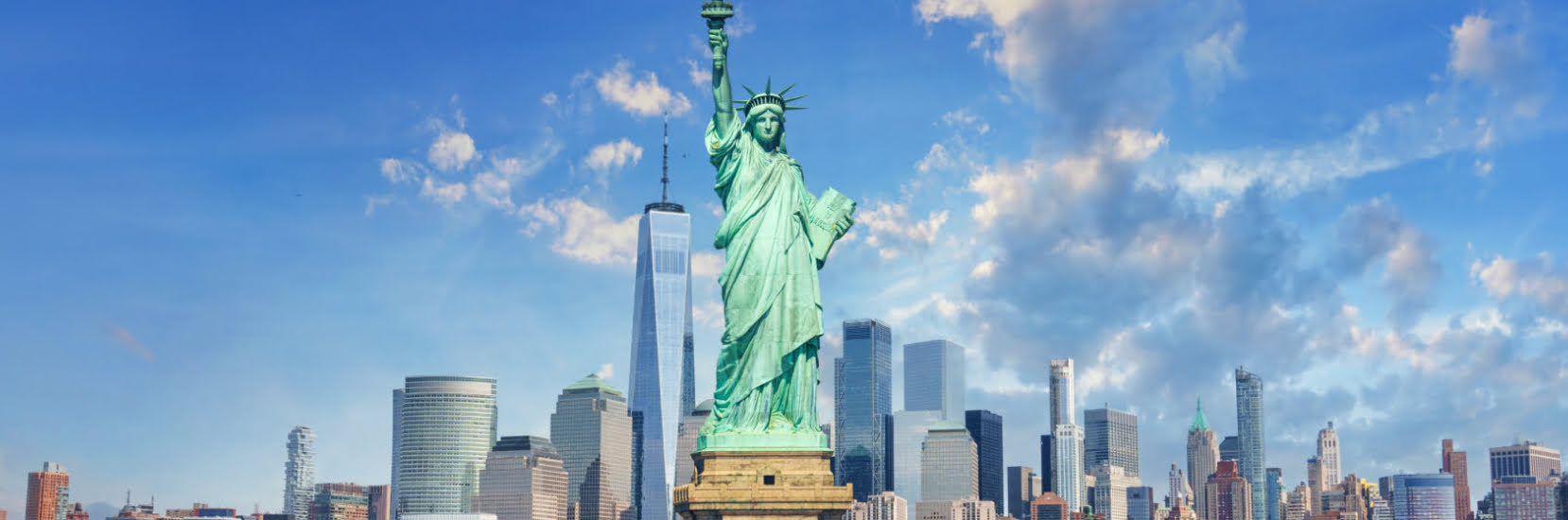 Statue of Liberty in front of the New York City skyline under a bright blue sky — a popular destination highlighting the importance of USA travel insurance.