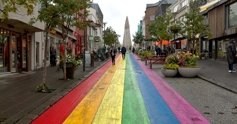 Rainbow Pride flag colours reflected across a diverse group of travellers at a European city pride event