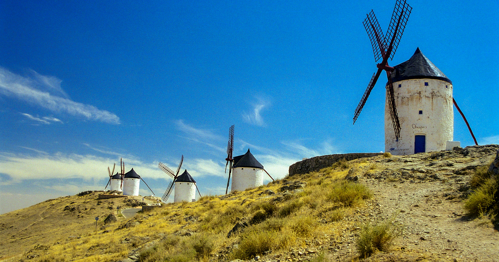 Traditional white windmills on a rocky hillside in La Mancha, Spain, under a bright blue sky — iconic rural landscape.