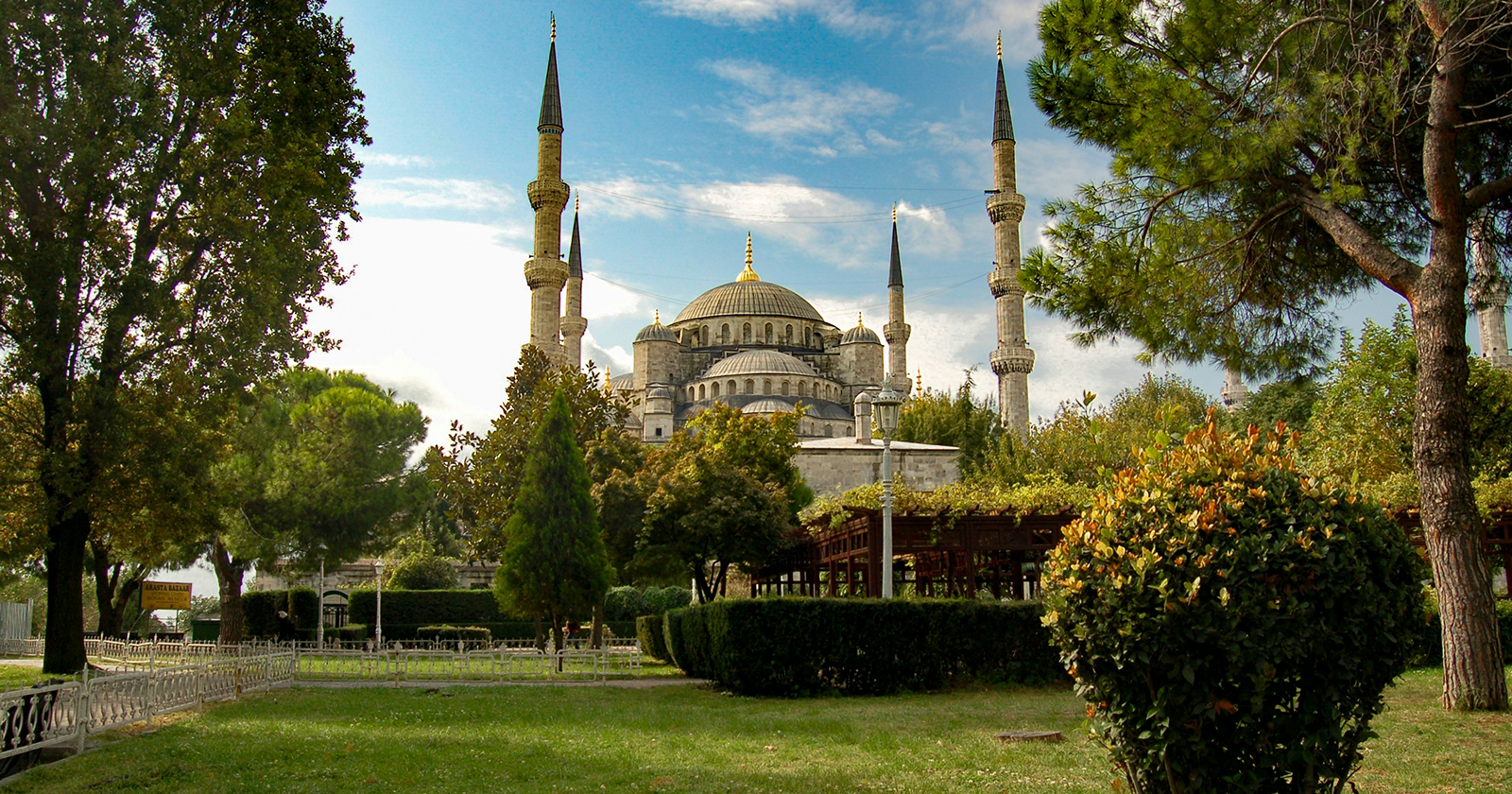 The Blue Mosque in Istanbul surrounded by green gardens and tall minarets under a bright blue sky.