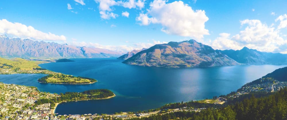 Panoramic view of Queenstown and Lake Wakatipu, surrounded by dramatic mountains beneath a bright blue sky in New Zealand.