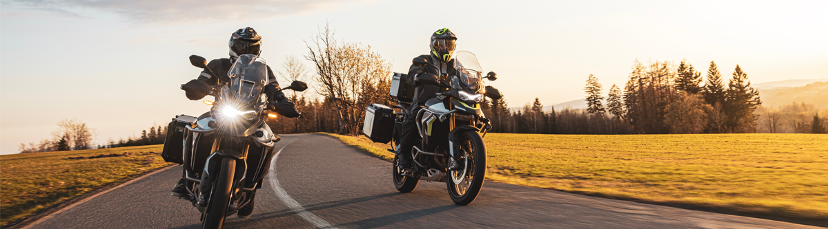Zwei Menschen fahren jeweils auf einem Motorrad nebeneinander über eine Landstraße in der Abendsonne