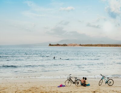 Menschen mit Fahrrad am Sandstrand mit Blick auf gegenüberliegende Landschaft