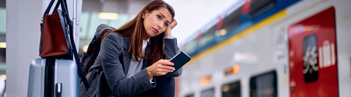 Frau mit Gepäck und dem Smartphone in der Hand wartet auf ihren Zug.