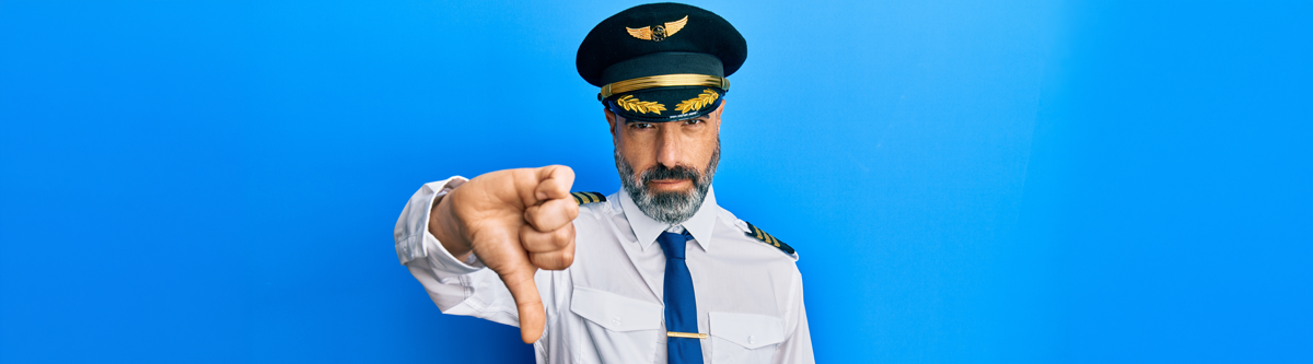 Flugzeugkapitän steht vor einem blauen Hintergrund und zeigt einen Daumen nach unten.