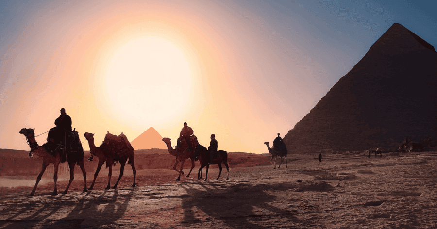 sunset view with people camel riding by the pyramids