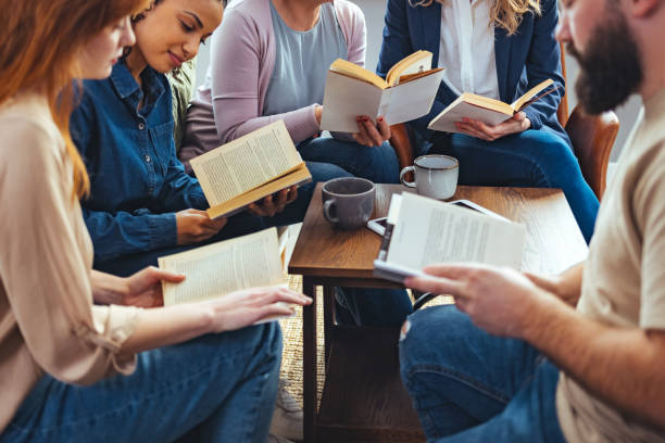 Group of people sitting in a circle reading books with coffee mugs on the table — casual book club meeting in a cozy indoor setting.